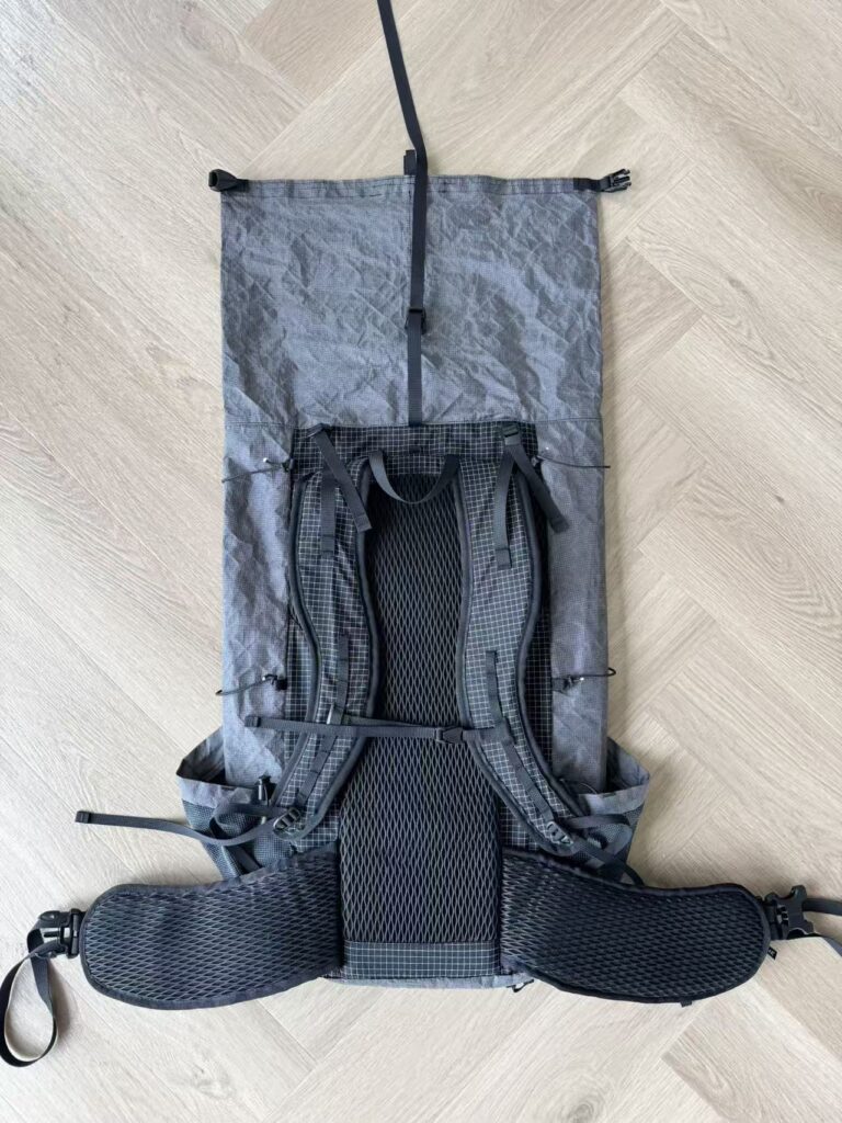 Light gray hiking backpack laid flat on a wooden floor, with padded shoulder straps, a waist belt, and a breathable back panel.