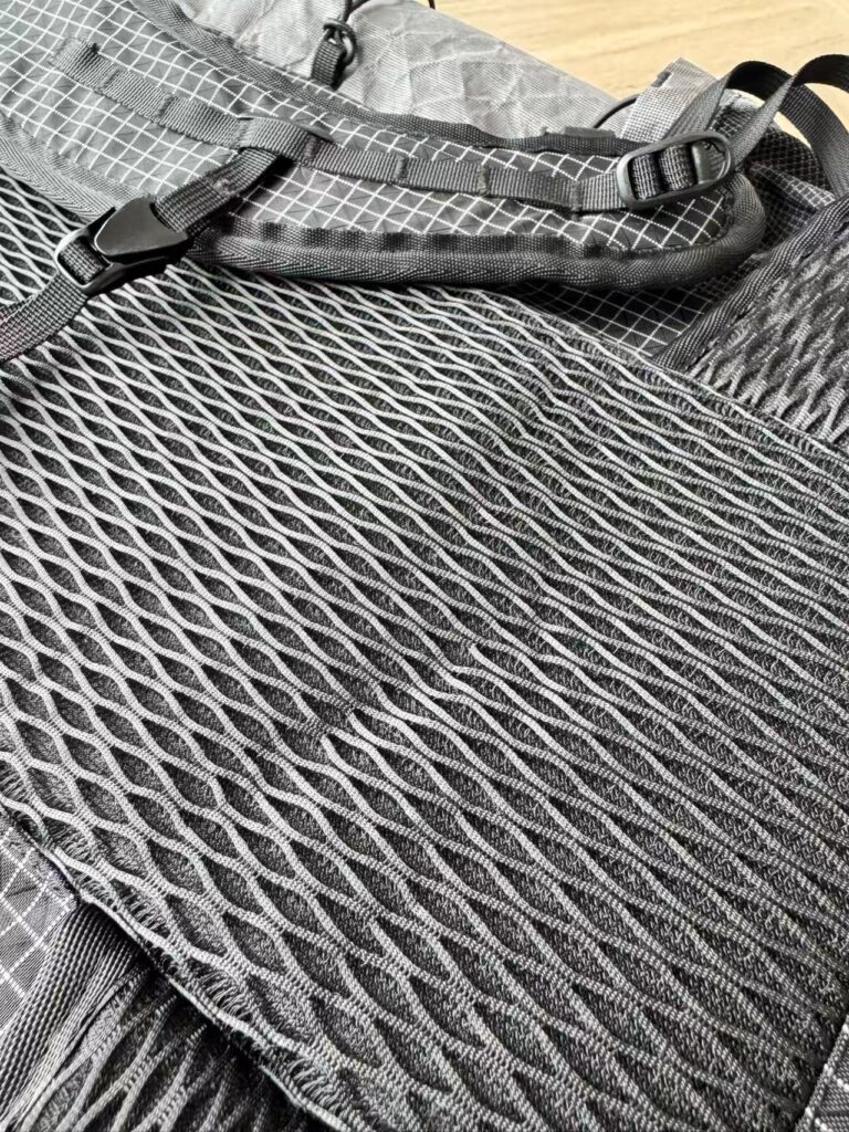 Close-up of a grey backpack with diamond-pattern mesh, straps and buckles.