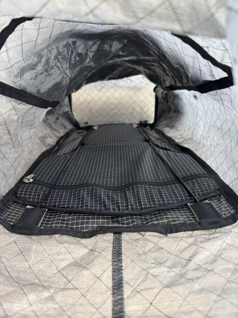 Interior view of a gray, diamond-patterned backpack opened to reveal padded compartments and mesh pockets along the bottom edge.